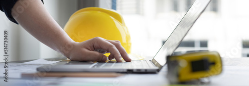 Young man with a laptop plotting a system of building structures in blueprints, Architects or engineers are designing buildings using computers to calculate the physical structure to be correct.