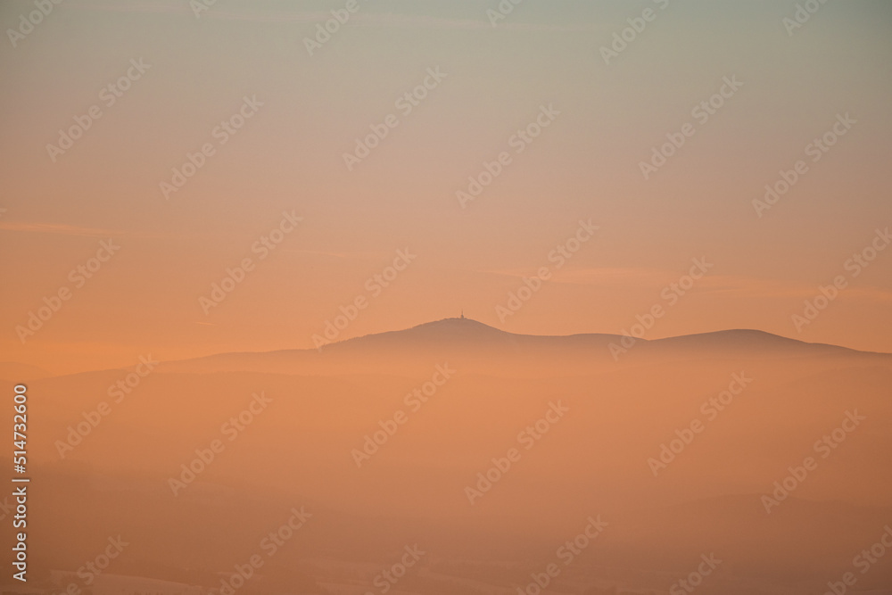 Obraz premium Frosty and foggy morning on the Polish Ochodzita mountain with a view of the Czech Beskydy mountains. Lysa mountain illuminated with orange light. Winter and frosty environment