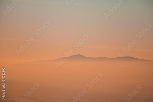 Frosty and foggy morning on the Polish Ochodzita mountain with a view of the Czech Beskydy mountains. Lysa mountain illuminated with orange light. Winter and frosty environment