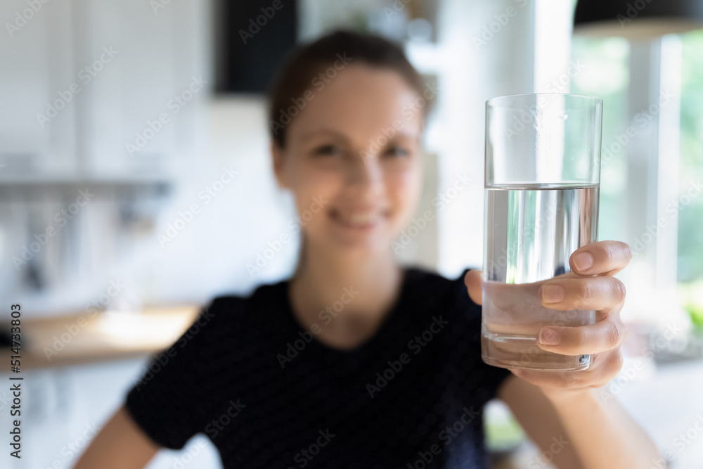 Happy healthy young woman promoting healthy daily routine habit, showing pure fresh water at camera, holding transparent glass, smiling, laughing, posing in home kitchen. Object close up Happy healthy young woman promoting healthy daily routine habit, showing pure fresh water at camera, holding transparent glass, smiling, laughing, posing in home kitchen. Object close up