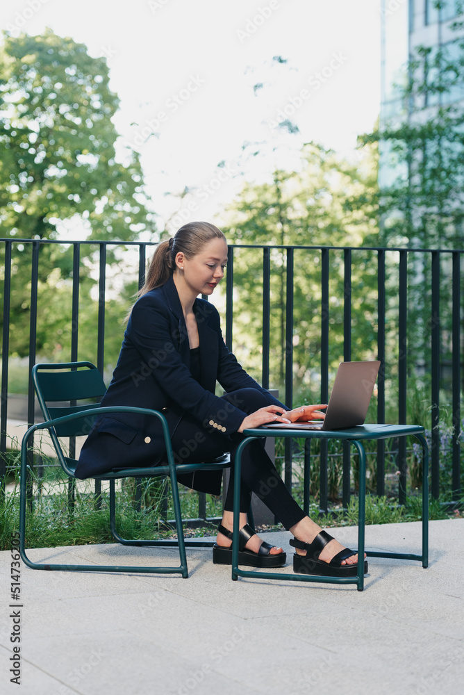 A female realtor in a blazer is working on a laptop in a modern urban space A female realtor in a blazer is working on a laptop in a modern urban space