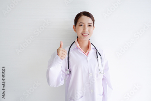 A smiling  beautiful Asian female doctor puts a stethoscope on her shoulder. wearing a white robe on a white background.