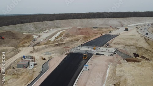 yellow truck pouring bitumen over a new road. Aerial drone shot. Road construction in progress on slope nature canyon. Infrastructure development and logistics.