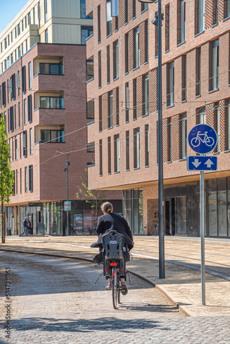 Girl or woman riding a bike on a road bike with blue road sign or signal of bicycle lane between modern buildings and offices in the center of Odense, Denmark, vertical