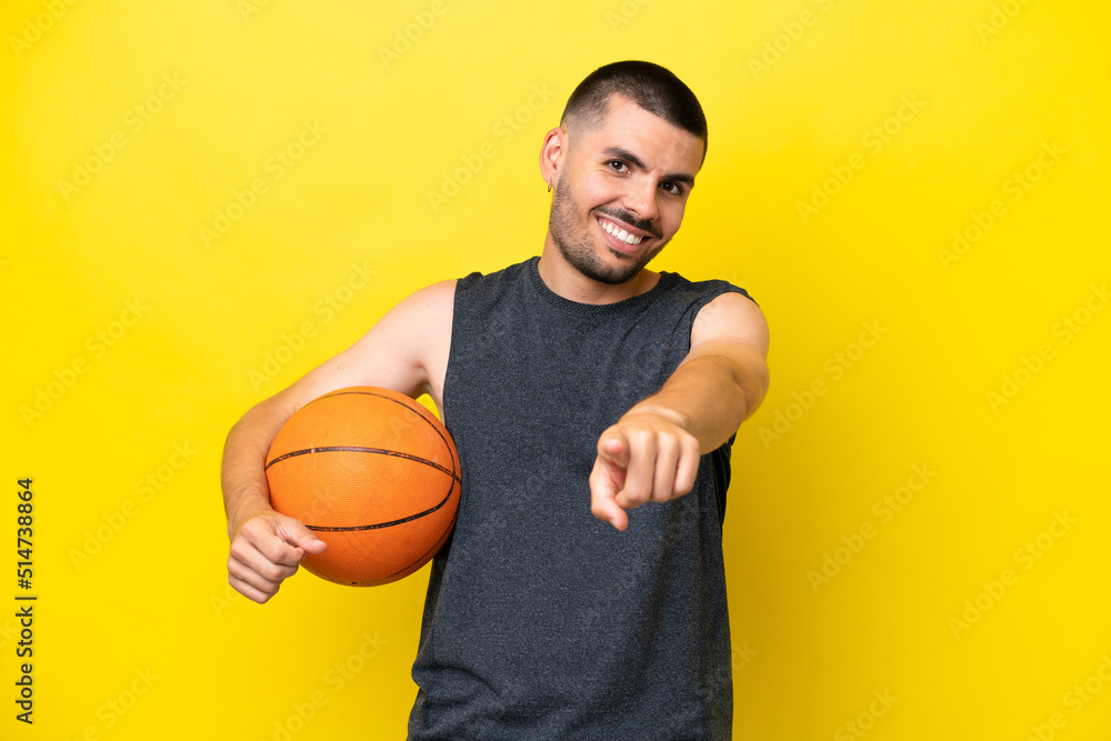 Young caucasian basketball player man isolated on yellow background pointing front with happy expression