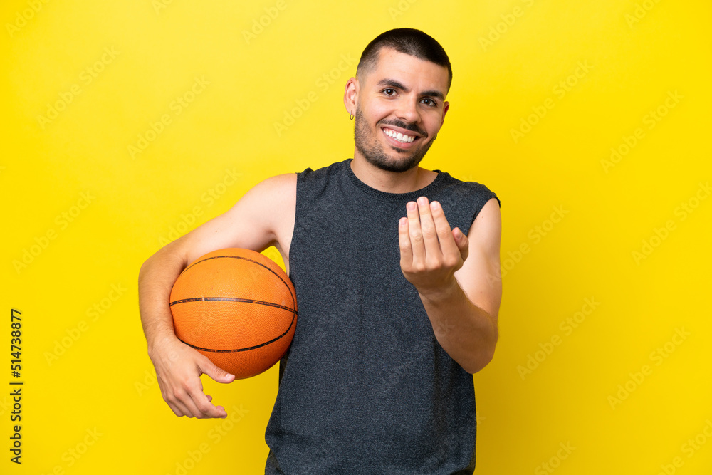 Young caucasian basketball player man isolated on yellow background inviting to come with hand. Happy that you came