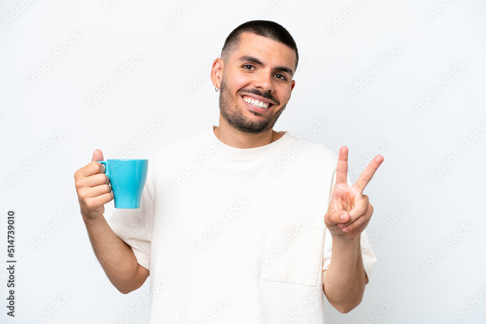 Young caucasian man holding cup of coffee isolated white background smiling and showing victory sign Young caucasian man holding cup of coffee isolated white background smiling and showing victory sign