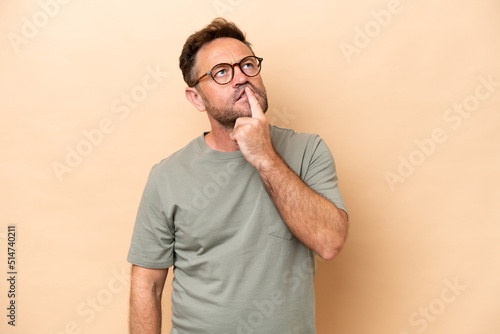 Middle age caucasian man isolated on beige background having doubts while looking up