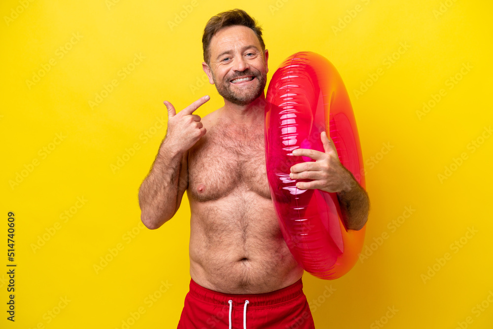Middle age caucasian man holding inflatable donut isolated on yellow background giving a thumbs up gesture