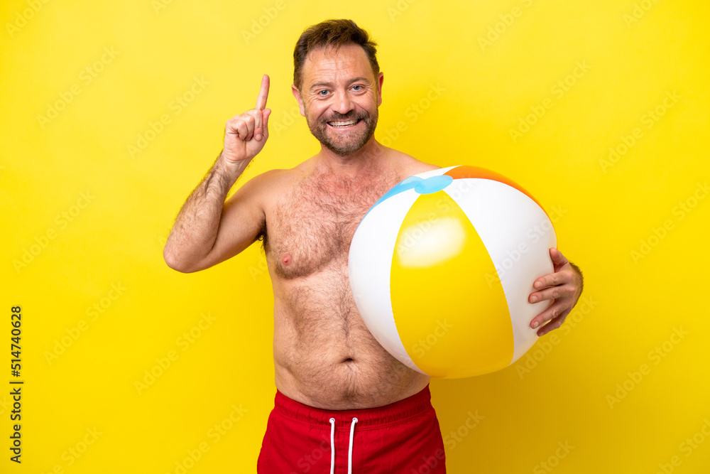 Middle age caucasian man holding beach ball isolated on yellow background pointing up a great idea