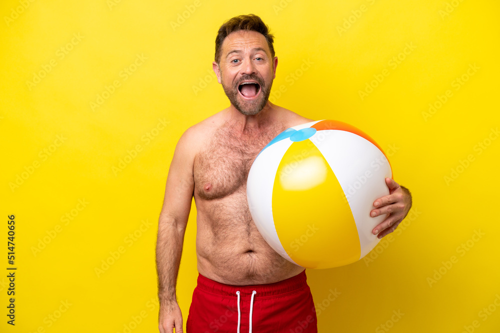 Middle age caucasian man holding beach ball isolated on yellow background with surprise facial expression