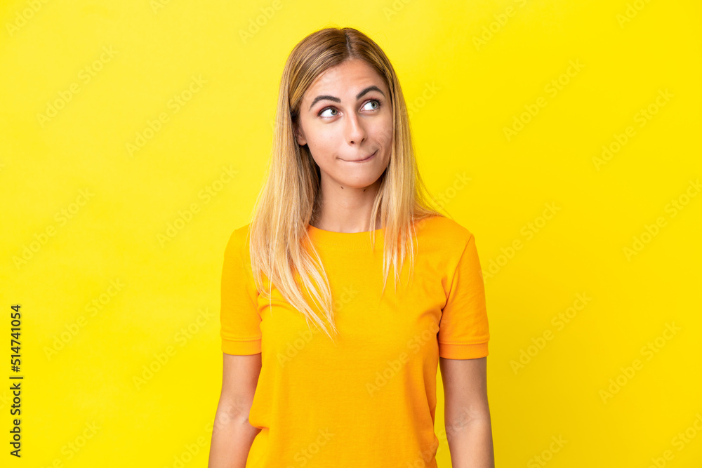 Blonde Uruguayan girl isolated on yellow background having doubts while looking up Blonde Uruguayan girl isolated on yellow background having doubts while looking up