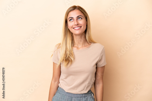Blonde Uruguayan girl isolated on beige background thinking an idea while looking up