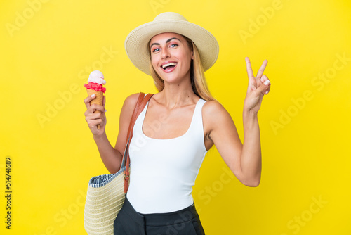 Blonde Uruguayan girl in summertime holding ice cream isolated on yellow background smiling and showing victory sign © luismolinero