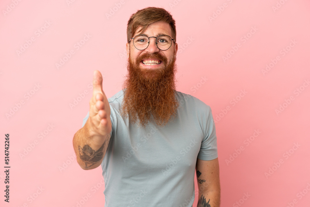 Young reddish caucasian man isolated on pink background shaking hands for closing a good deal Young reddish caucasian man isolated on pink background shaking hands for closing a good deal