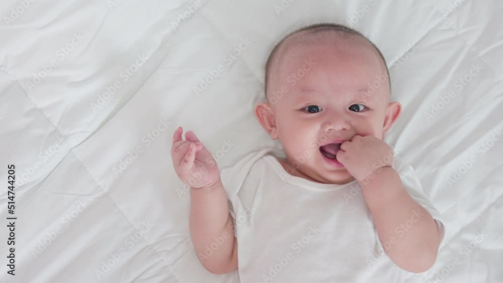Portrait of cute asian newborn baby lying play on white bed look at camera with laughing smile happy face. Innocent little new infant adorable. Parenthood and Mother Day concept. Portrait of cute asian newborn baby lying play on white bed look at camera with laughing smile happy face. Innocent little new infant adorable. Parenthood and Mother Day concept.