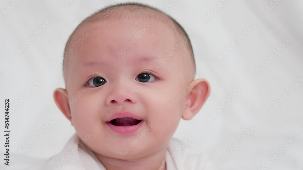 Close-up of face cute asian newborn baby lying play on white bed look at camera with laughing smile happy face. Innocent little new infant adorable. Parenthood and Mother Day concept. Close-up of face cute asian newborn baby lying play on white bed look at camera with laughing smile happy face. Innocent little new infant adorable. Parenthood and Mother Day concept.