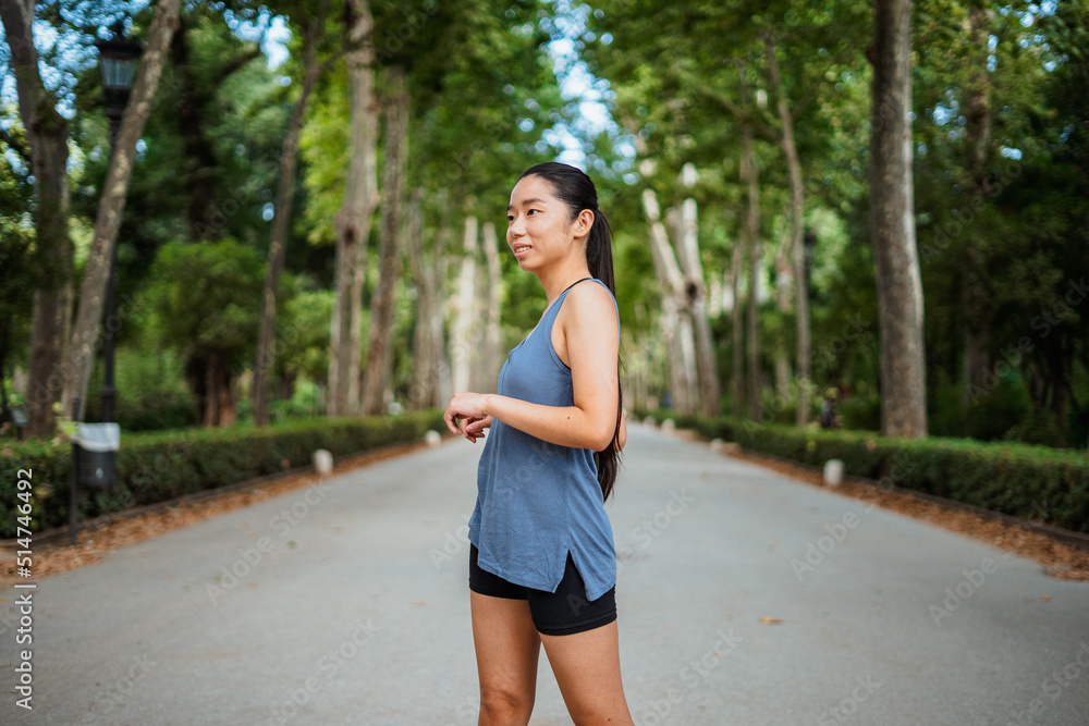 Cheerful asian sport girl warming up in the park before jogging