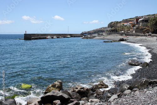 A rugged coastal scene with blue water and rocks and a blue cloudy sky