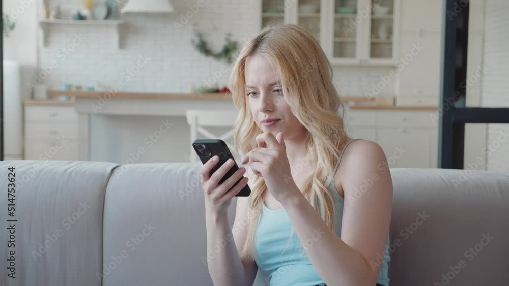 Millennial woman sit on sofa holding smartphone read great news on sms feels overjoyed, clenched fist makes yes gesture looking very happy. Auction betting victory, personal achievement, candid Millennial woman sit on sofa holding smartphone read great news on sms feels overjoyed, clenched fist makes yes gesture looking very happy. Auction betting victory, personal achievement, candid