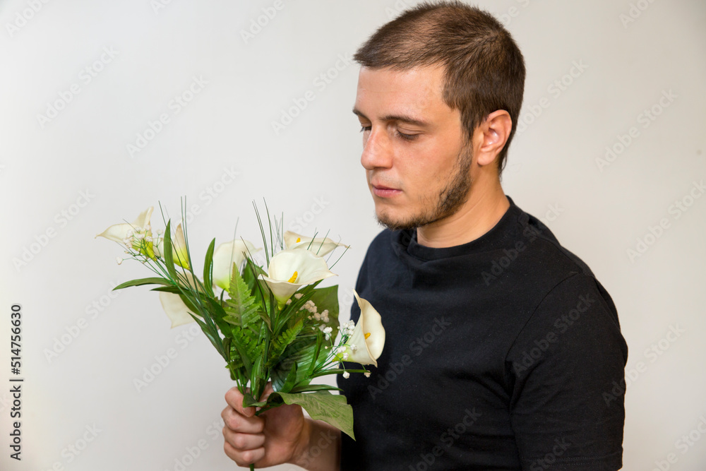 Young boy in love with a bouquet of white flowers of Zantedeschia aethiopica, commonly known as calla lily and arum lily. Young white caucasian man with short hair, little beard and dark eyes.