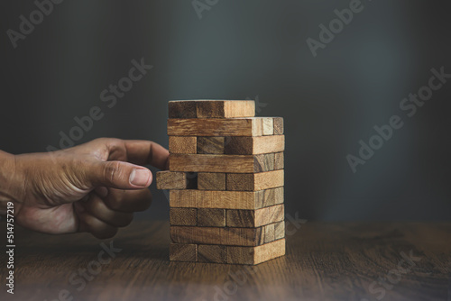 Hand placing wooden block tower stack in pyramid stair step with caution to prevent collapse or crash concepts of financial risk management and strategic planning and business challenge plan.