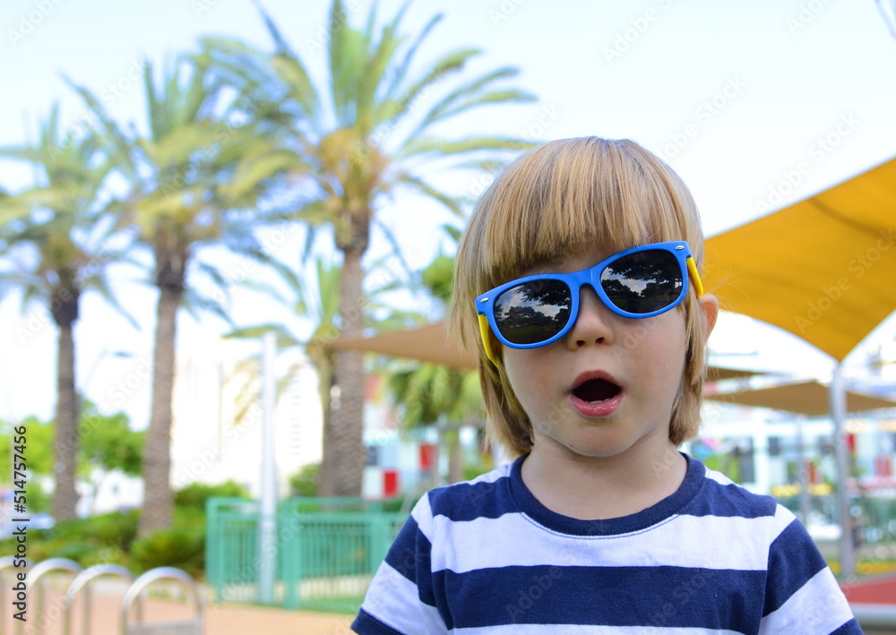 Funny child on the playground. Boy in sunglasses under palm trees. Preschooler playing outside, summer day Funny child on the playground. Boy in sunglasses under palm trees. Preschooler playing outside, summer day