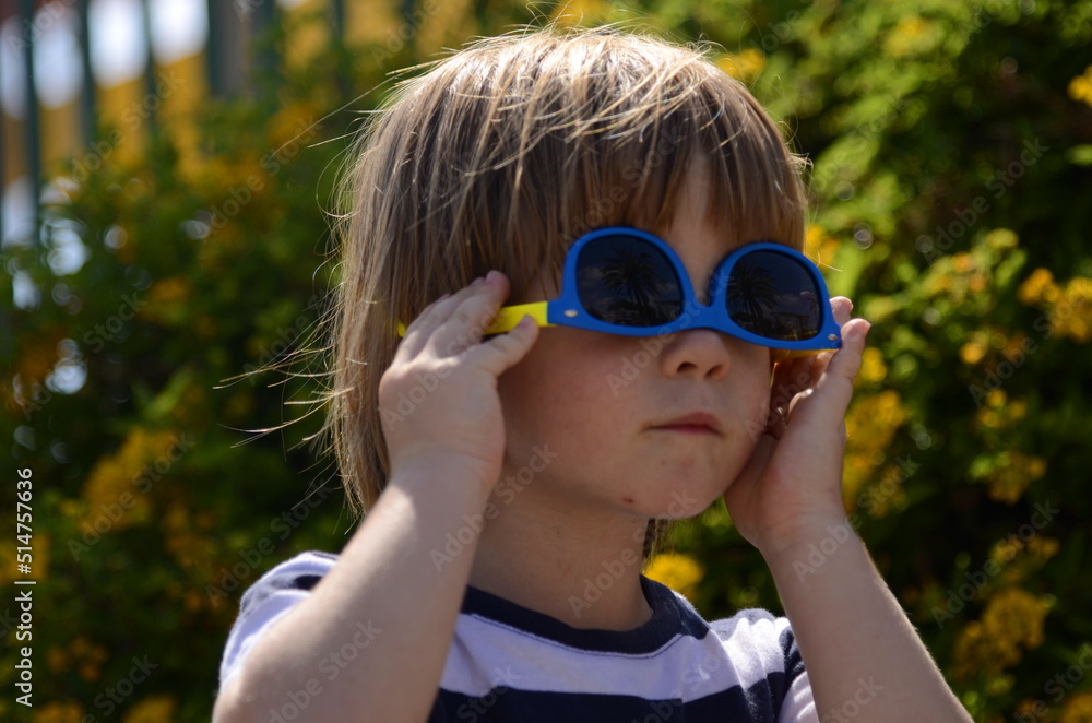 Portrait of a little boy in sunglasses. A child in front of a flowering bush. Concept: holidays, summer camp, kindergarten, family vacation, childhood. Funny kid Portrait of a little boy in sunglasses. A child in front of a flowering bush. Concept: holidays, summer camp, kindergarten, family vacation, childhood. Funny kid