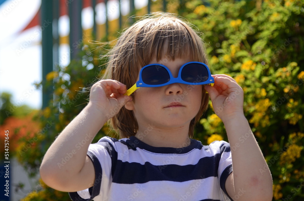 Portrait of a little boy in sunglasses. A child in front of a flowering bush. Concept: holidays, summer camp, kindergarten, family vacation, childhood. Funny kid Portrait of a little boy in sunglasses. A child in front of a flowering bush. Concept: holidays, summer camp, kindergarten, family vacation, childhood. Funny kid