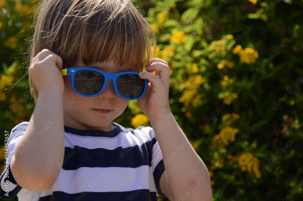 Portrait of a little boy in sunglasses. A child in front of a flowering bush. Concept: holidays, summer camp, kindergarten, family vacation, childhood. Funny kid Portrait of a little boy in sunglasses. A child in front of a flowering bush. Concept: holidays, summer camp, kindergarten, family vacation, childhood. Funny kid