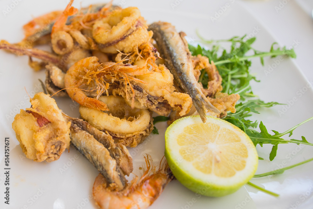 Fried local seafood (Fritto misto di mare or Fritto misto di pesce ) squid rings, prawns, sardines, and octopus, with lemon on white plate. Popular food in Sicily. 