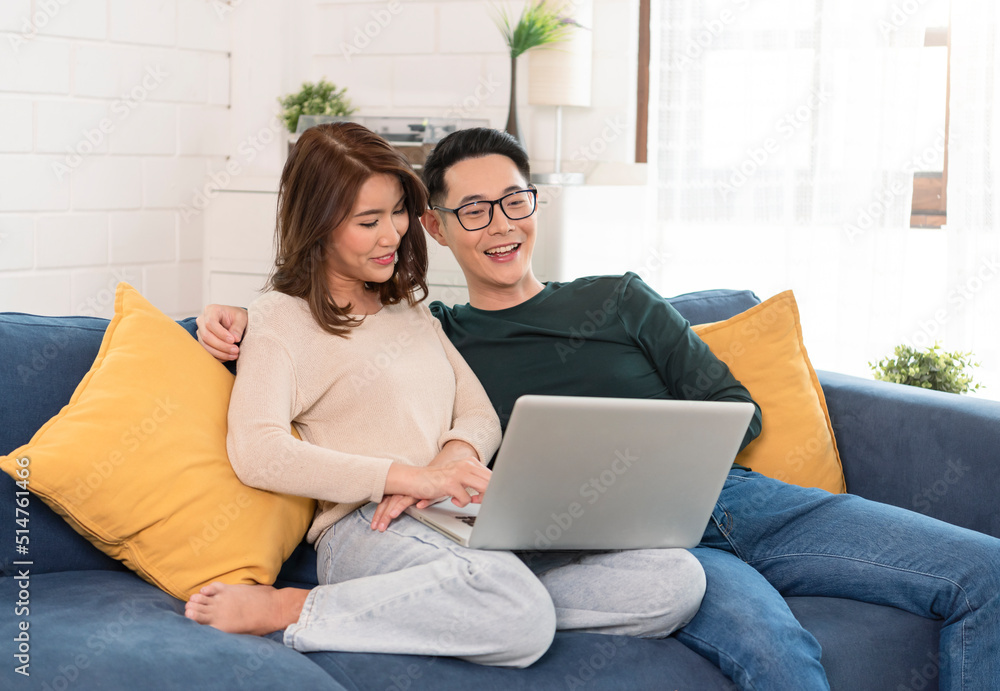 Asian couple watching movie in computer laptop together on sofa in living room at home. family lifestyle concept. Asian couple watching movie in computer laptop together on sofa in living room at home. family lifestyle concept.