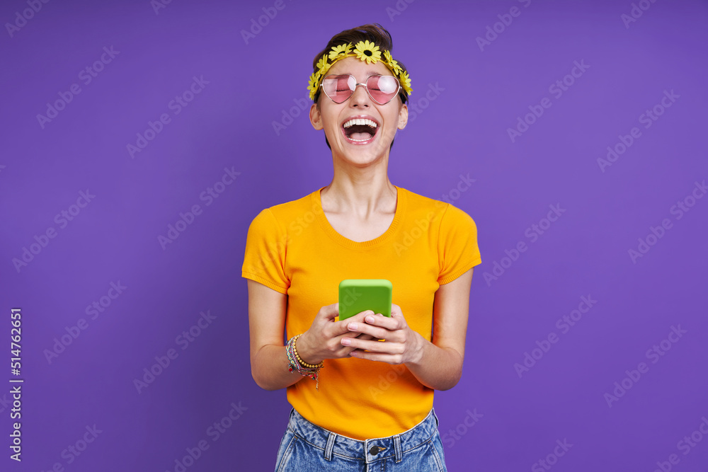 Excited woman holding smart phone while standing against purple background