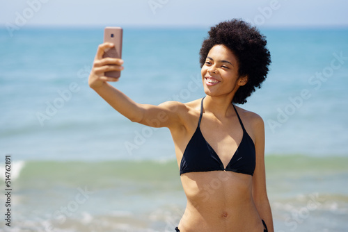 Black woman in bikini taking selfie near sea