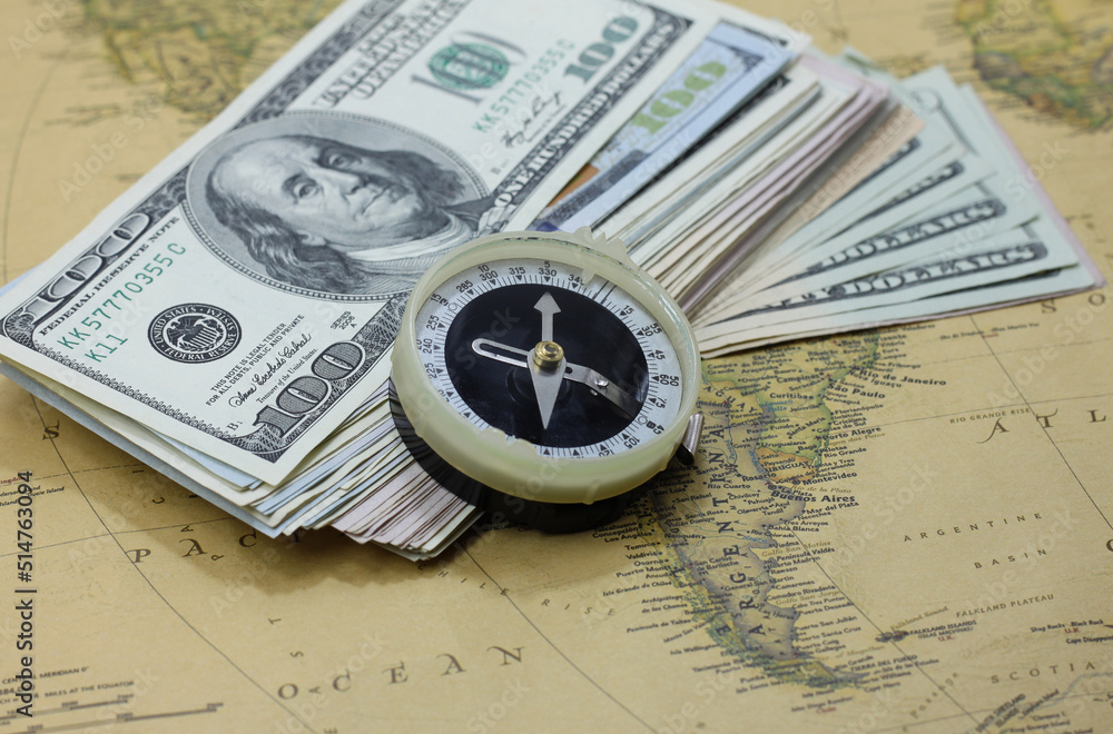 Classic round compass and american dollars on background of old vintage map of world as symbol of tourism with compass, travel with compass and outdoor activities with compass Classic round compass and american dollars on background of old vintage map of world as symbol of tourism with compass, travel with compass and outdoor activities with compass