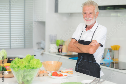 Happy smiling senior Caucasian man standing arms crossed in kitchen at home