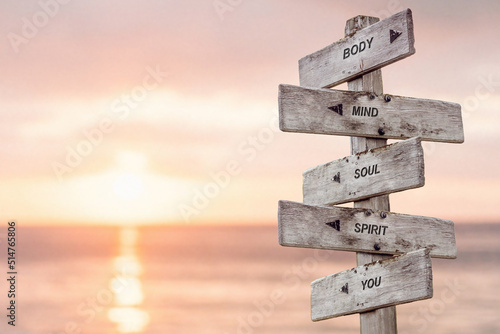 BODY MIND SOUL SPIRIT YOU text on wooden signpost outdoors by the beach at sunset