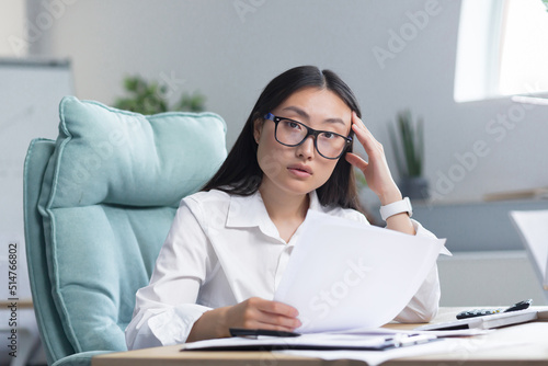Frustrated and upset asian business woman working in office, holding documents with bad and negative financial indicators of company, financier working. © Liubomir