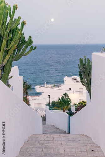 Full moon over the sea, viewed from a narrow street of a village with white houses on the Mediterranean coast