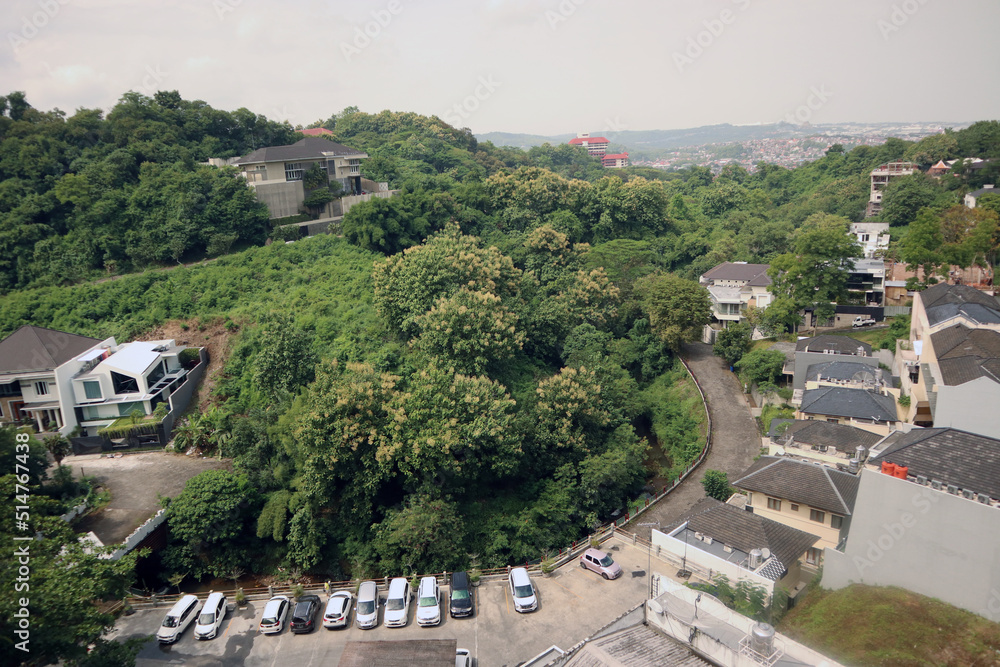 Fototapeta premium Cityscape buildings view from above with natural green forest trees mountain as part of the scenery