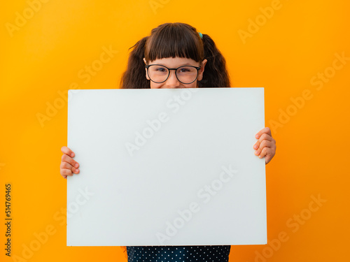 portrait of a brunette girl child with glasses schoolgirl girl child kid pointing finger on white poster banner isolated on yellow color background
