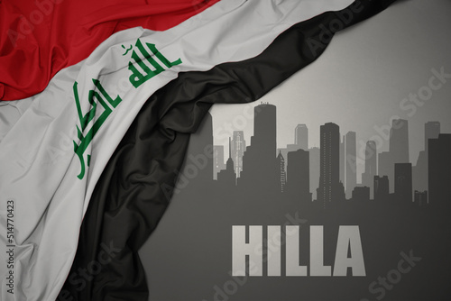 abstract silhouette of the city with text Hilla near waving national flag of iraq on a gray background.3D illustration photo