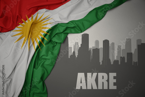 Bild auf Leinwand abstract silhouette of the city with text Akre near waving national flag of kurdistan on a gray background