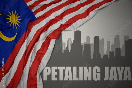 Fotografija abstract silhouette of the city with text Petaling Jaya near waving national flag of malaysia on a gray background