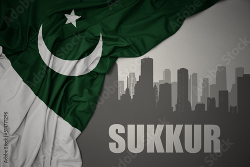 abstract silhouette of the city with text Sukkur near waving national flag of pakistan on a gray background.3D illustration photo