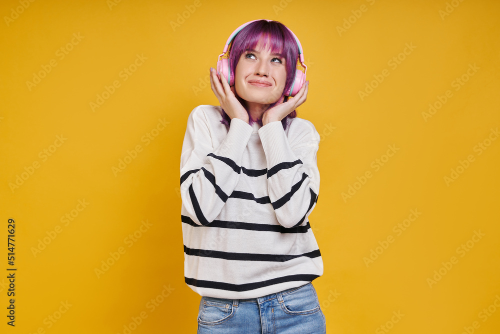 Joyful young woman adjusting headphones while standing against yellow background Joyful young woman adjusting headphones while standing against yellow background