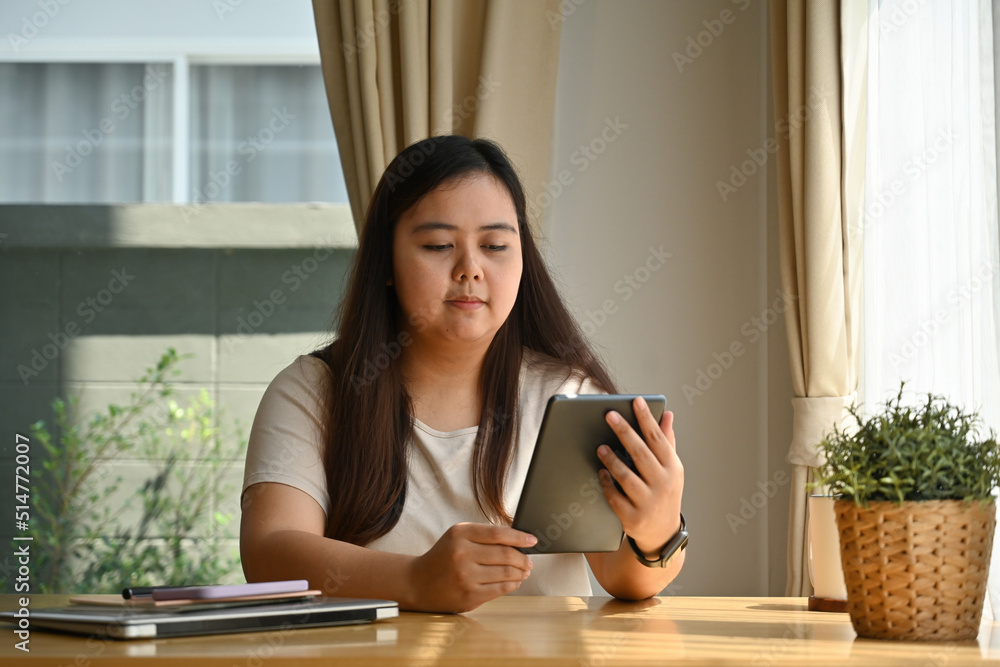 Beautiful plus size woman using tablet while sitting in the office desk, Domestic life, Studying from home concept. Beautiful plus size woman using tablet while sitting in the office desk, Domestic life, Studying from home concept.
