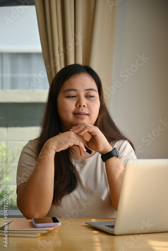 Beautiful chubby young woman working with laptop at home office, sitting at desk in front of open laptop computer, Domestic life, Studying from home concept.