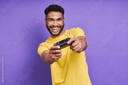 Playful African man holding joystick while standing against purple background