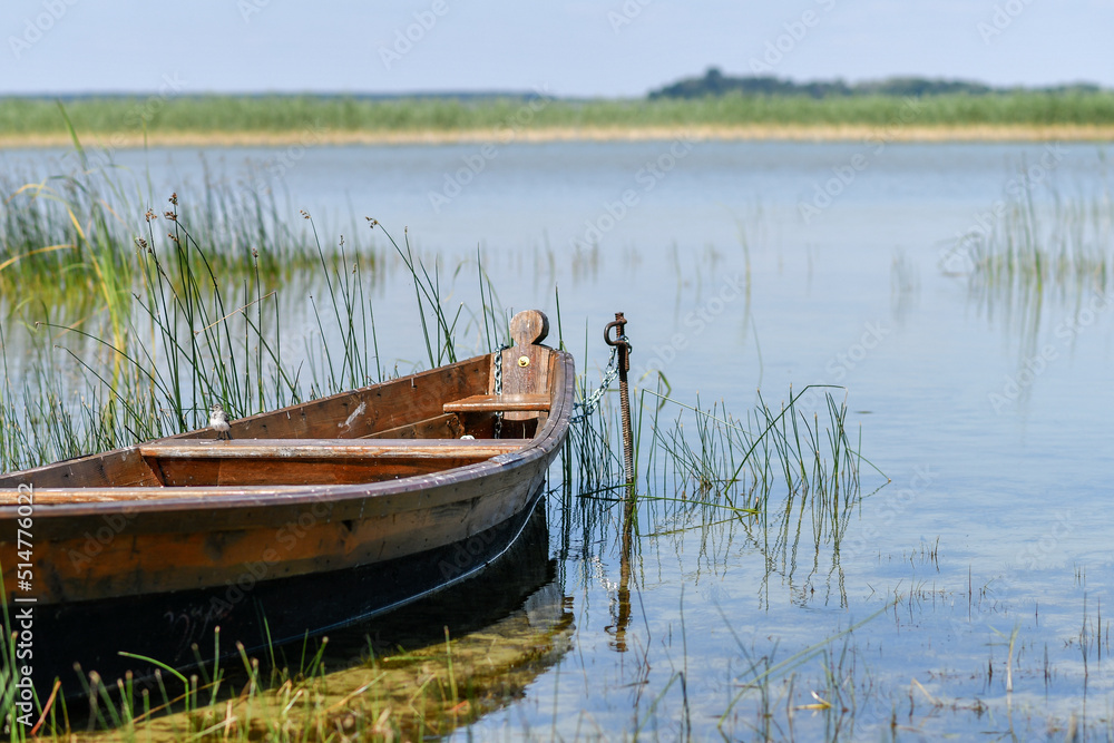 Fragment of wooden fishing boat on the lake with transparent blue sky and clear water.